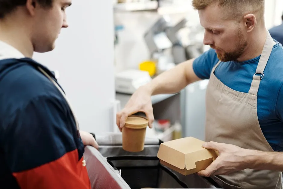 A server handing a paper takeaway container and cup to a customer at a quick-service restaurant counter
